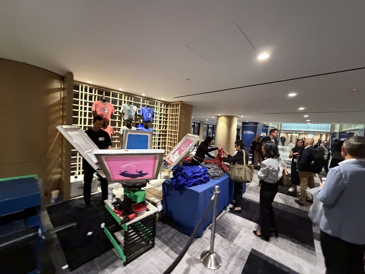 Full screen-print carousel press set up in a hotel lobby with a line of guests at the merch table